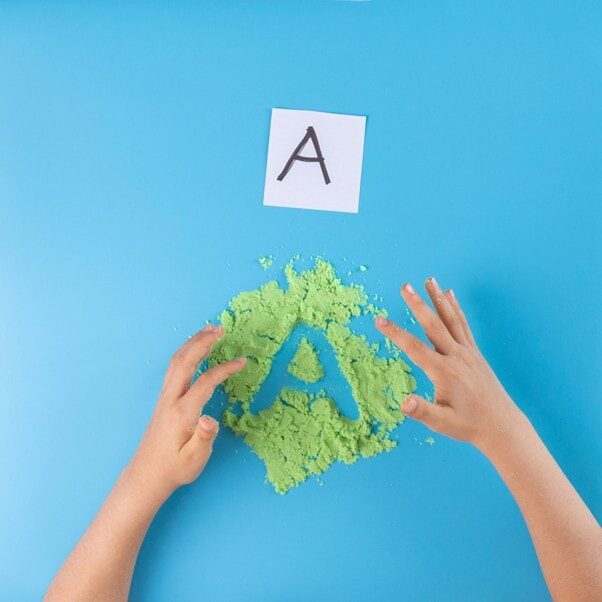 Childs hands drawing an A in kinetic sand
